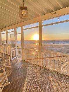 a porch with chairs and hammock on the deck overlooking the ocean at sunset