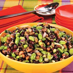 a yellow bowl filled with beans and other food on top of a colorful table cloth