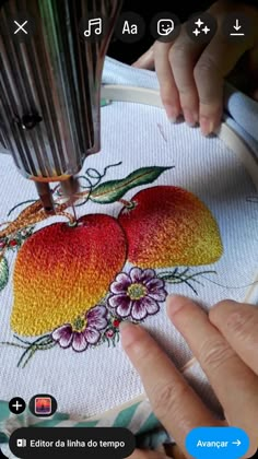 someone is working on an embroidery project with flowers and fruit in the center, while another person's hands are using a sewing machine to sew