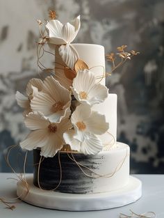 a three tiered cake with white flowers on top and gold accents around the edges