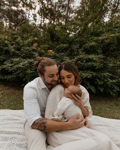 a man and woman are sitting on a blanket while holding a baby in their arms