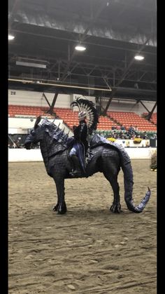 a man riding on the back of a black horse in an indoor arena at a rodeo