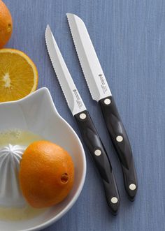 two oranges are in a white bowl and some knives