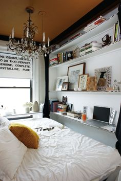 a white bed sitting under a chandelier in a bedroom next to a window