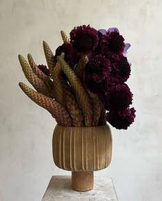 a vase filled with purple flowers sitting on top of a white table next to a wall