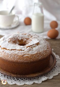 a cake sitting on top of a wooden plate covered in powdered sugar next to eggs