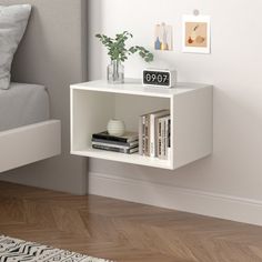 a white shelf next to a bed with books and vases on top of it