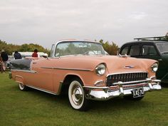 an old car is parked on the grass near other cars and people are standing around