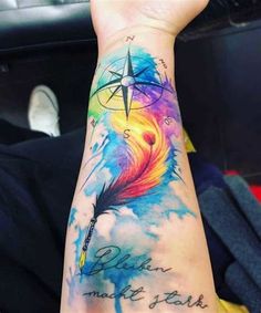 a person with a colorful tattoo on their arm holding a compass and rainbow ink in the sky