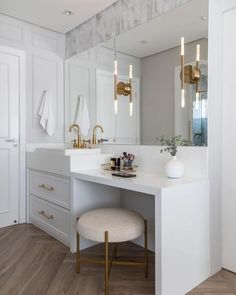 a white bathroom with gold accents and marble counter tops, along with two stools