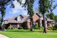 a large brick house with lots of trees in the front yard and landscaping around it