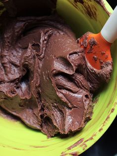 a yellow bowl filled with chocolate frosting and an orange spoon in it's center