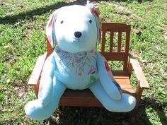 a blue teddy bear sitting on top of a wooden chair in the middle of grass