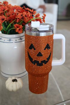 an orange pumpkin mug sitting on top of a glass table next to a vase with flowers