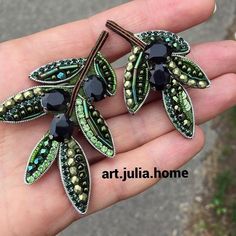 two green and black brooches on a person's hand with the words art julia home