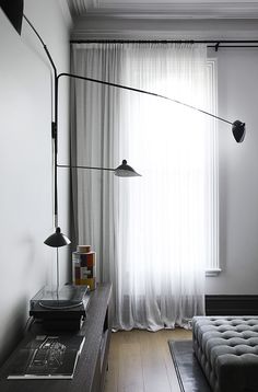 a living room with a couch, table and lamp next to a window that has white drapes on it