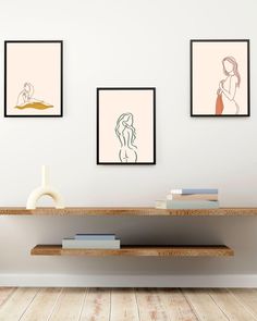 three framed art prints hang on the wall above a shelf in a room with wood flooring