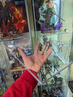 a person's hand reaching out from behind a glass display case filled with action figures