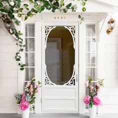 two white vases filled with flowers sitting in front of a door to a house