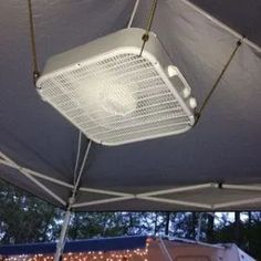 an air conditioner is suspended from the roof of a tent with string lights on it