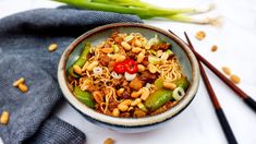 a bowl filled with noodles and vegetables next to chopsticks on a white surface