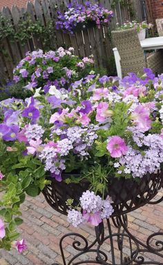 purple and white flowers are in a basket on a metal stand next to a brick patio