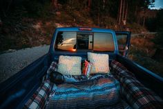 the back end of a truck with pillows and blankets in it's bed on the side of the road