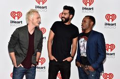 three men standing next to each other in front of a red heart radio wall with the words iheart radio on it