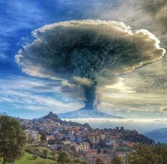 a very large cloud is in the sky over a small town on a hill with trees