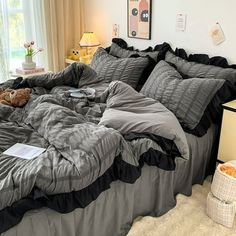 an unmade bed with grey and black comforter in a bedroom next to a window