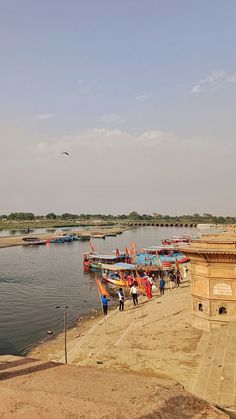 several boats are docked on the shore by the water's edge as people walk near them