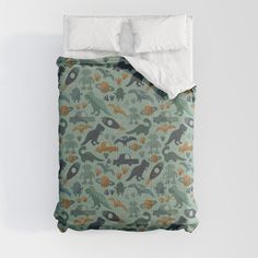 a bed covered in a green and orange dinosaur print comforter with two pillows on top