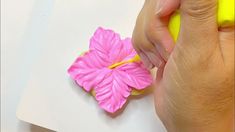 a hand is holding a yellow marker over a pink flower