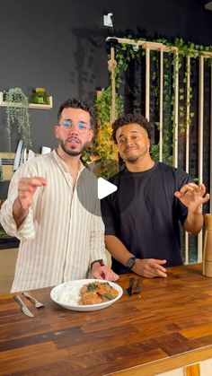 two men standing in front of a table with food on it and one holding a knife