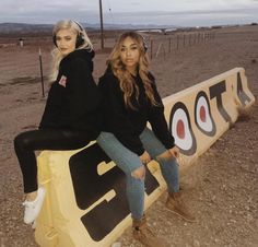 two women sitting on top of a sign in the desert