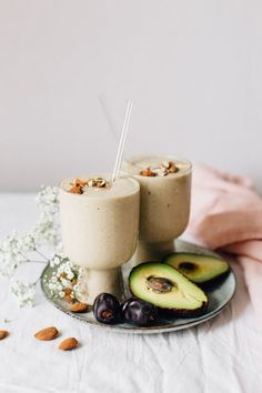 two smoothies on a plate with an avocado and almonds