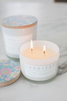 two candles sitting next to each other on top of a white table with coasters