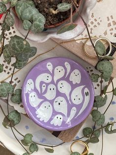 a purple plate with ghost faces painted on it next to some plants and gold scissors