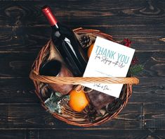 a thank card sitting on top of a basket filled with fruit and wine bottles next to a bottle of wine