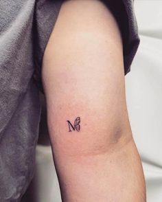 a small butterfly tattoo on the right arm and shoulder, with an upper letter m in black ink