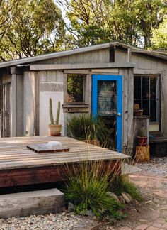 a small wooden house with a blue door and cactus in the front yard, surrounded by rocks