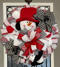 a snowman wreath on the front door with a red hat and black and white bow