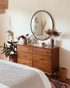 a bedroom with a dresser, mirror and potted plants on it's side