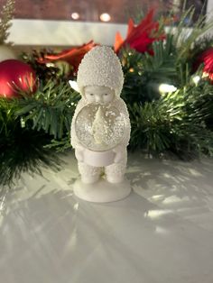 a small white figurine sitting on top of a table next to christmas decorations