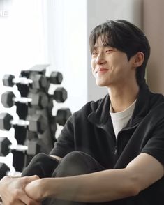 a young man sitting in front of a stack of dumbbells