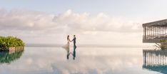 a bride and groom standing on the edge of a pool