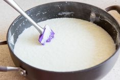 a pan filled with white liquid and a purple spatula sticking out of the top