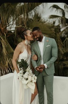 a bride and groom kissing in front of palm trees