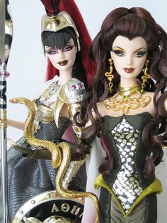 two dolls are dressed in costumes and holding swords, one has a snake on her arm