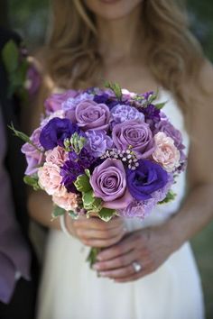 a bride holding a bouquet of purple and pink flowers